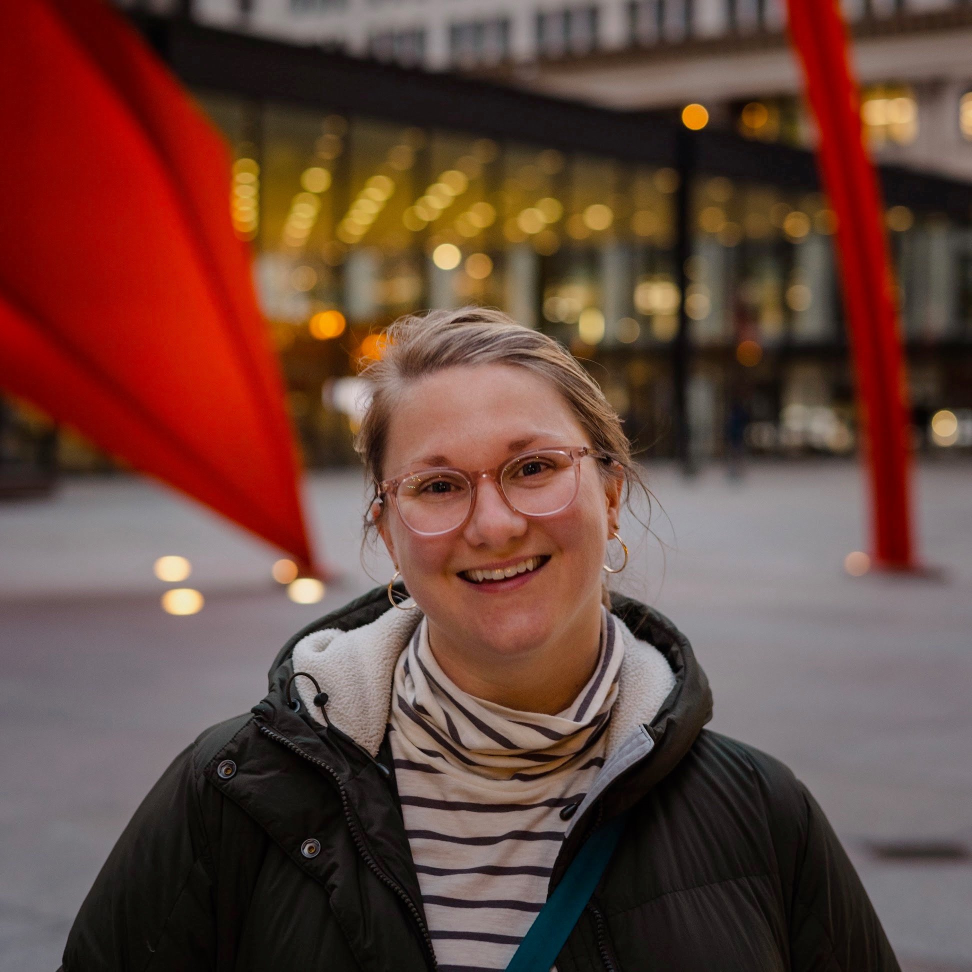 Meagan Estep, smiling, in glasses and a striped turtleneck, in front of a red steel sculpture